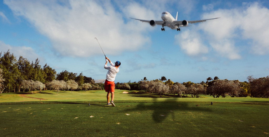 golfer hitting a golf shot with a plane flying above