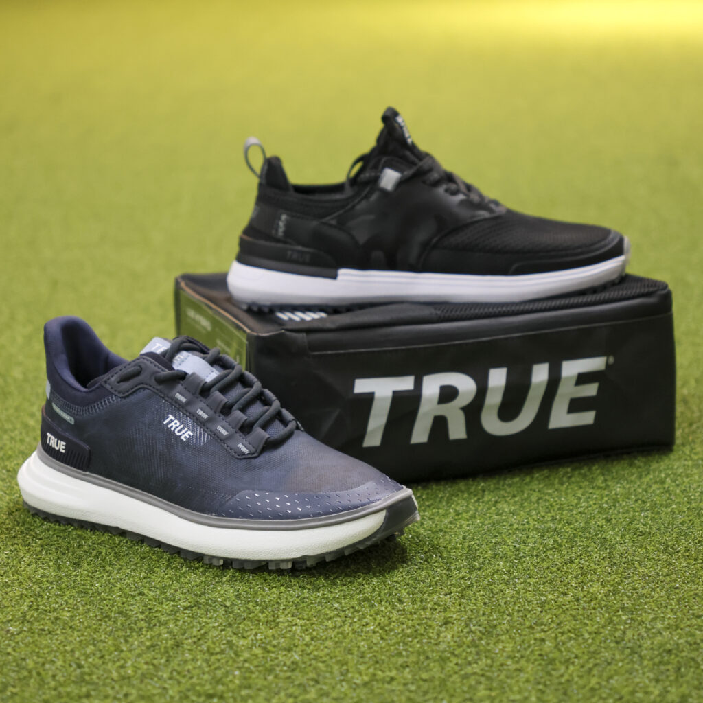 Two knit TRUE shoes on a green with a TRUE shoebox.
